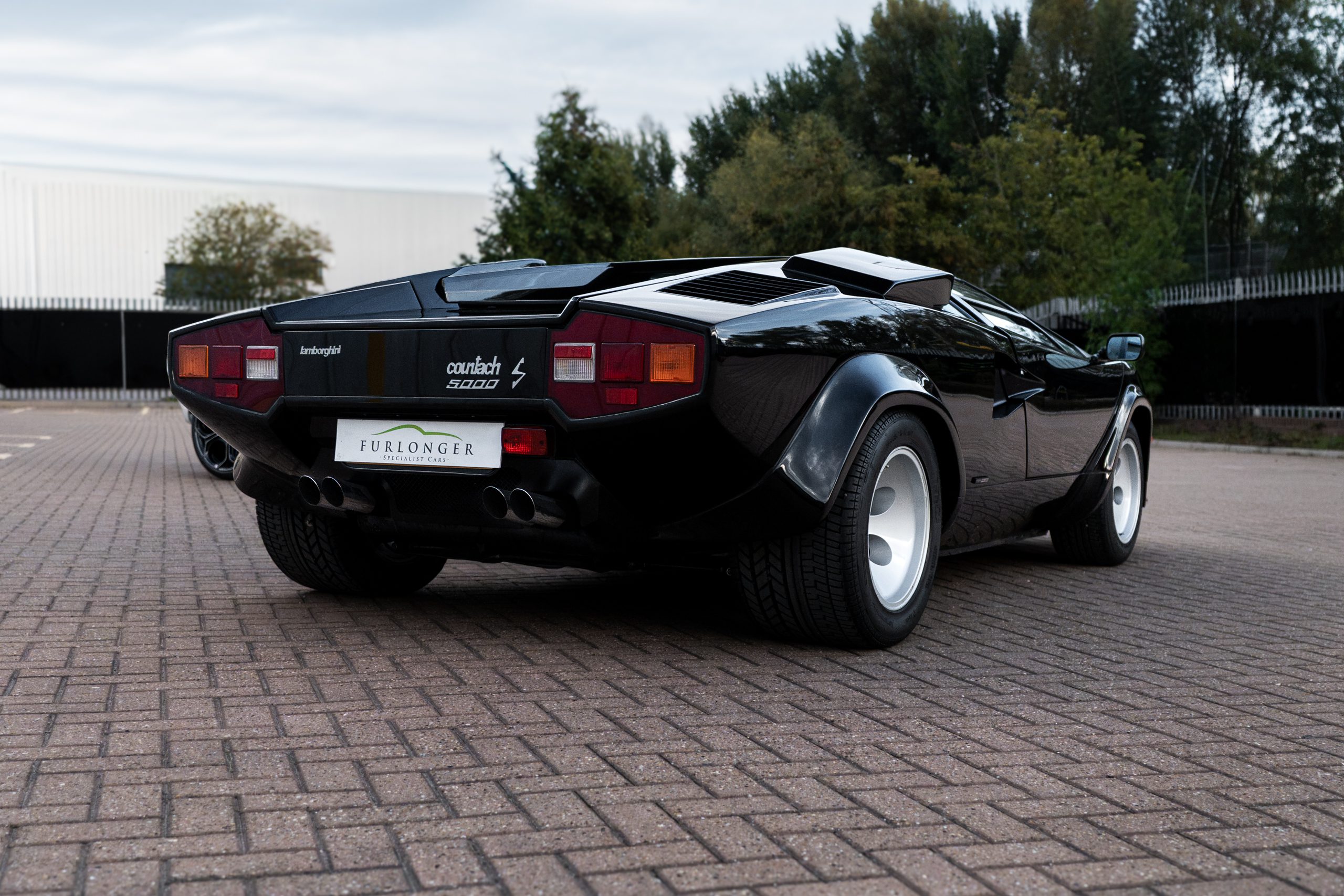 Rear three-quarter view of the black Countach 5000 S showing its “countach 5000 S” badging, red and amber tail lights, quad exhausts and wide rear arches.
