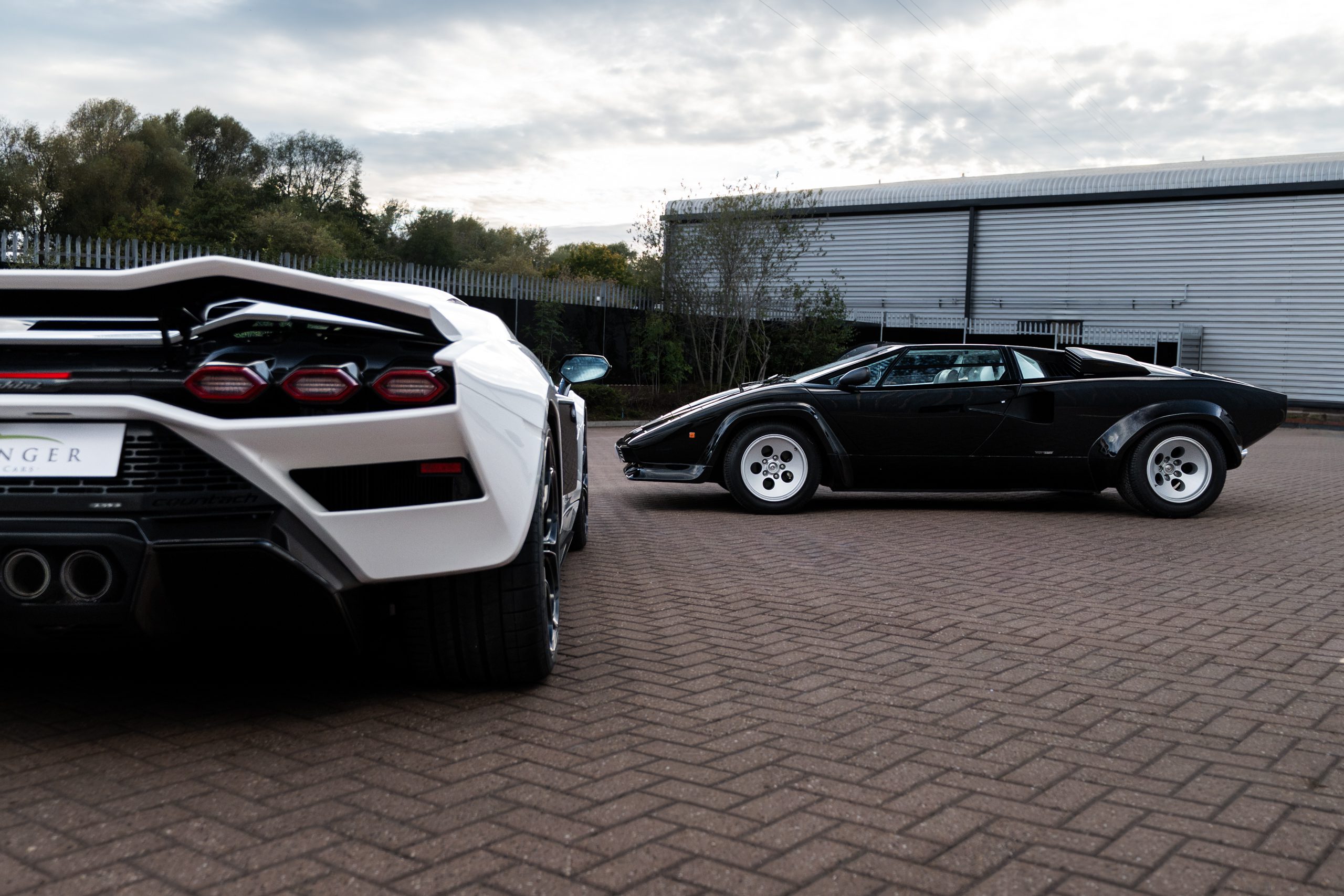Rear of the white Countach LPI 800-4 with its hexagonal tail lights and quad exhausts, and the black Countach 5000 S in side profile behind it.